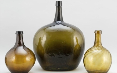 THREE GLASS DEMIJOHNS One olive green, height 17", and two amber with swirled necks, heights 11".