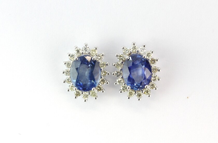 A pair of 18ct white gold (stamped 750) cluster earrings set with an oval cut sapphire surrounded by brilliant cut diamonds, L. 1.3cm.