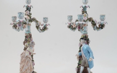A pair of Sitzendorf figural four-light candelabra, blue underglaze marks, each modelled with a floral encrusted tree-trunk stem and male and female figure, supporting floral encrusted branches with flowerhead sconces, each 52cm high (2)