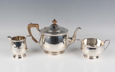 A George V silver three-piece tea set, each piece of circular form with foliate rim, on a stepped ci