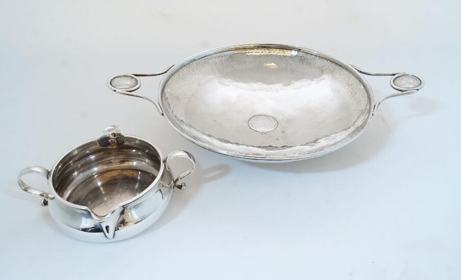 A planished silver twin handled shallow bowl, Birmingham, 1917, Albert Edward Jones, with inset George III coin to centre and two Queen Anne coins inset to handles, on circular foot, numbered 663 to underside, 25.9cm wide; together with a late...