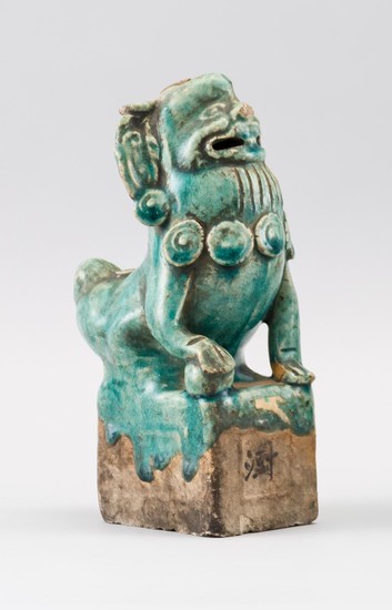 CHINESE POTTERY FIGURE OF A FU DOG Seated on a square plinth and with a brocade ball under his paw. Turquoise glaze. Wax seal on its...