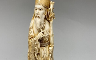 JAPON, c. 1940. Okimono en ivoire sculpté, représentant un sage barbu debout, tenant un bâton,...