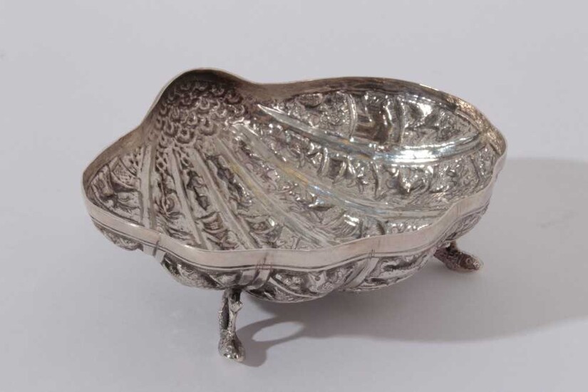 Late 19th / early 20th century Burmese silver dish of shell form, with embossed decoration, raised on three feet modelled as coiled fish, (Unmarked) All at approximately 2.5oz 10.5cm in diameter.