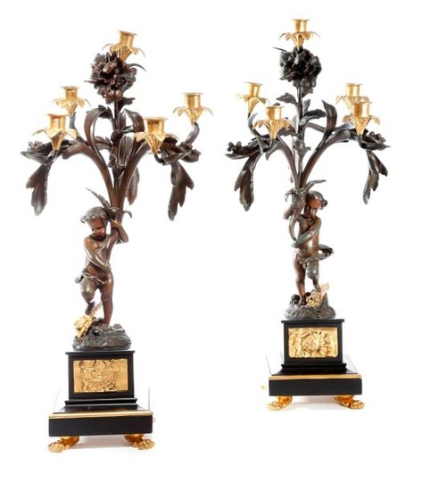 A PAIR OF FRENCH GILT AND PATINATED BRONZE FIGURAL CANDELABRA IN LOUIS XV STYLE, EARLY 20TH CENTURY each in the form of a putto supporting leaves and flowers, with five lights with flowerhead drip-pans and urn nozzles, on black marble bases inset with...