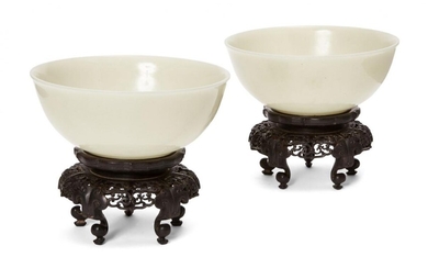 A pair of Chinese pale celadon jade bowls, 19th century, each carved with deep sides and a slightly everted mouth rim, base with an incised apocryphal Qianlong mark, 17.5 cm diameter wide, both on finely carved openwork hardwood stands