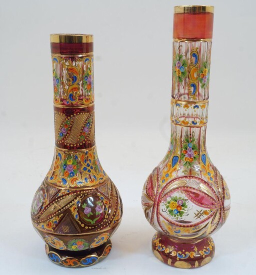 Two Bohemian clear and ruby glass bottle vases, 19th century, each with gilded rims, the bodies enamelled with floral sprays and cut glass geometric panels and patterns surrounded with gilded highlights, atop gilded and enamelled glass bases...