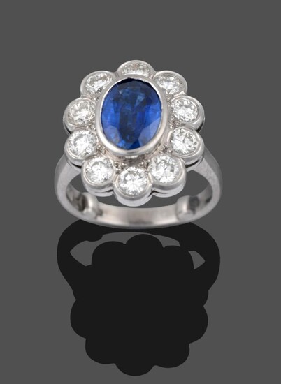 A Platinum Sapphire and Diamond Cluster Ring, the oval mixed cut sapphire in a rubbed over...