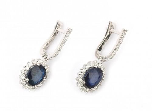 A pair of 14 karat white gold sapphire and diamond cluster earrings. Featuring an oval cut blue sapphire of ca. 1 ct. in a surround of sixteen brilliant cut diamonds. The upper part also set with brilliant cut diamonds. In total ca. 0.60 ct., ca. G-H...