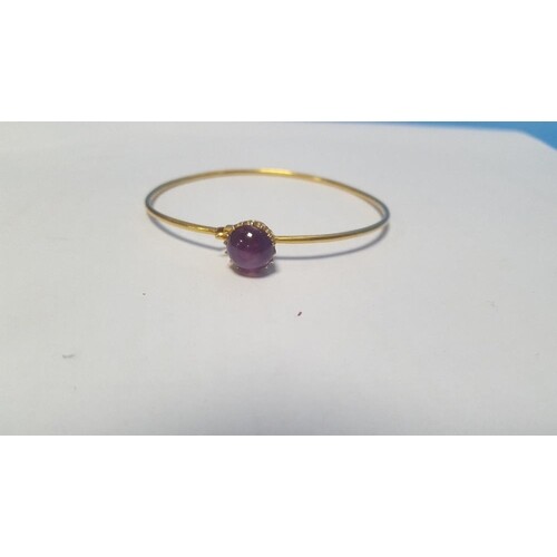 AN UNMARKED YELLOW METAL BANGLE SET WITH A PURPLE CABACHON P...