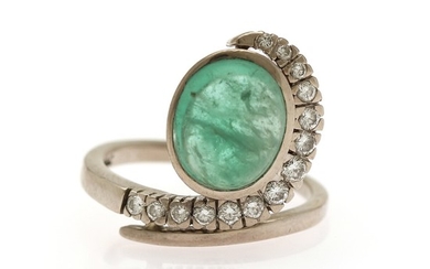 An emerald and diamond ring set with a cabochon emerald flanked by numerous diamonds, mounted in 18k white gold. Size 50.