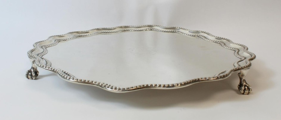 Silver circular tray with wavy beaded and moulded edge on cl...