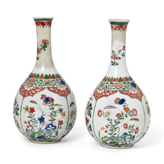 A pair of Chinese porcelain bottle vases, Kangxi period, painted in famille verte enamels with panels of flowering peony, chrysanthemum and lily blossoms emerging from rockwork, all beneath a band of leafy scrolls and flower heads, the neck...