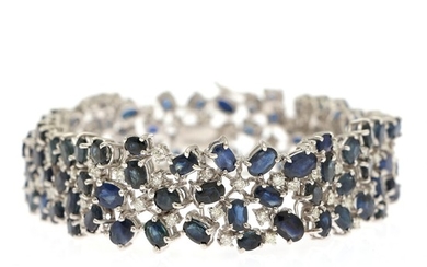A sapphire and diamond bracelet set with numerous oval-cut sapphires and brilliant-cut diamonds, mounted in 14k white gold.