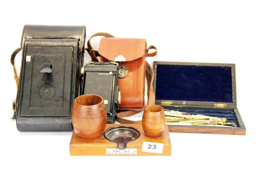 A smoker's stand with bakelite ashtray made from the teak of HMS Ajax, together with two cameras and a case of drawing instruments.