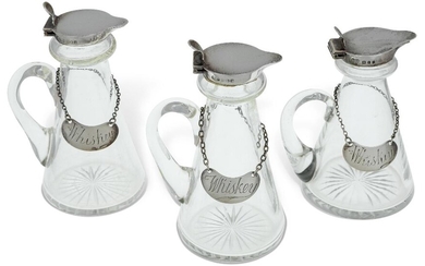 Three silver mounted whisky noggins comprising a pair Birmingham, 1933, William Suckling, 11.5cm high, and a slightly smaller example, London, 1920, Goldsmiths & Silversmiths Co., 10.5cm high, all three with conical glass bodies and hinged covers...