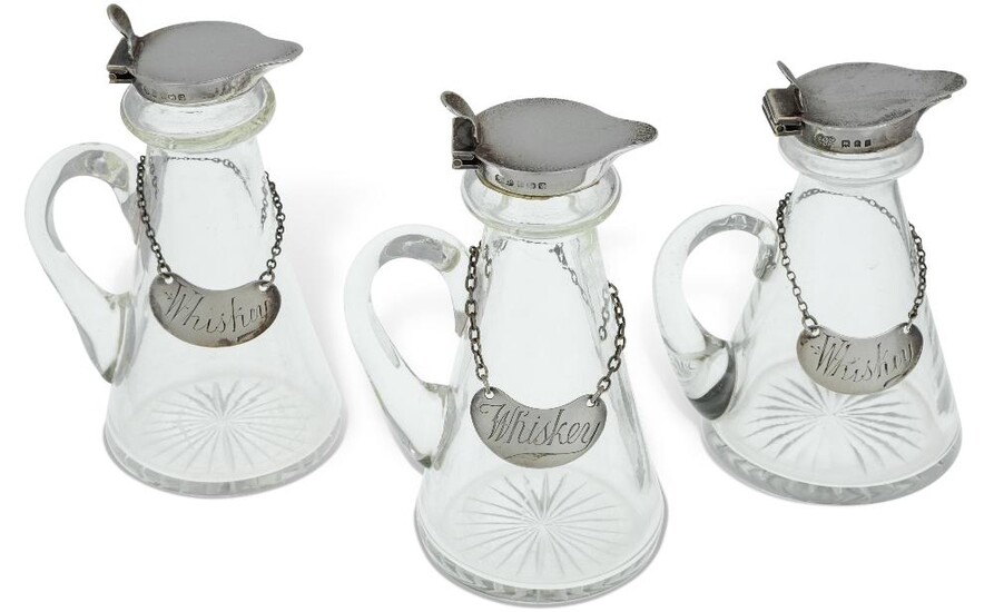 Three silver mounted whisky noggins comprising a pair Birmingham, 1933, William Suckling, 11.5cm high, and a slightly smaller example, London, 1920, Goldsmiths & Silversmiths Co., 10.5cm high, all three with conical glass bodies and hinged covers...