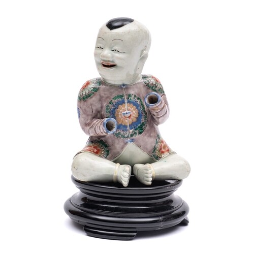 A Chinese famille verte seated figure of a smiling boy: wear...
