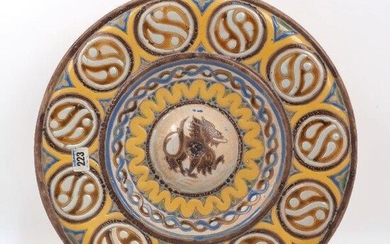 A Continental pottery charger, late 19th century, of Hispano-Moresque form and decorated with coloured slip, the raised central boss with a wyvern enclosed by waved and interwoven bands, the border with eleven circular panels, the footrim pierced...