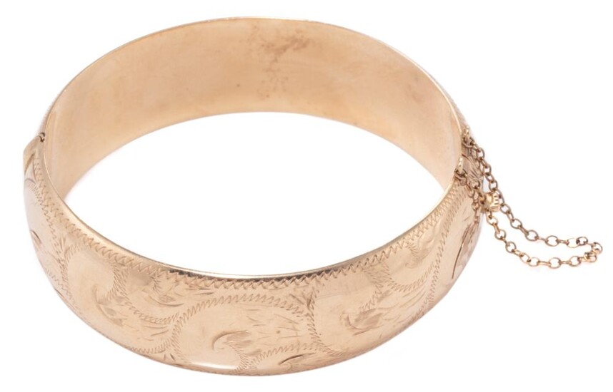 A 9CT GOLD ENGRAVED HINGED BAGLE; 19mm wide hollow bangle with scrolling engraving and safety chain, internal circ. 18cm, wt. 30.98g.