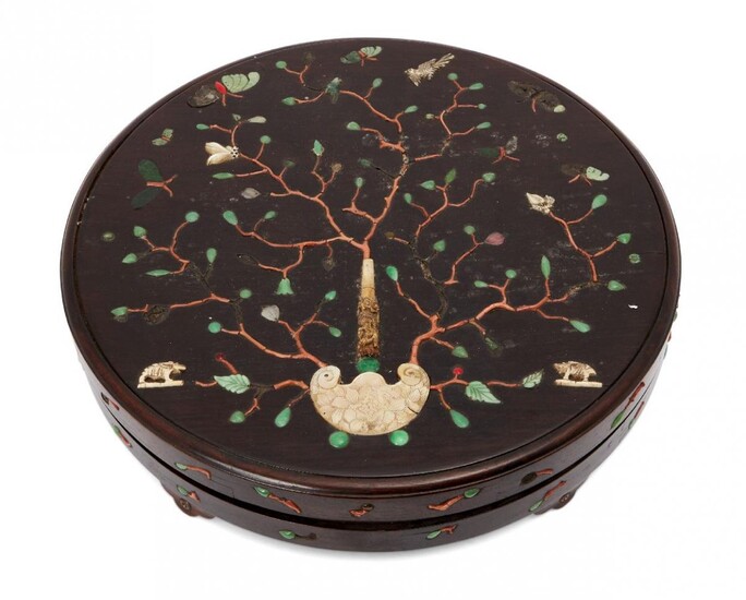 A Chinese hardwood circular box and cover, 18th century, inlaid with a carved ivory handle issuing hardstone branches ending with ivory and mother-of-pearl blossoms amidst jadeite buds, above a carved mother-of-pearl panel with incised flowering...