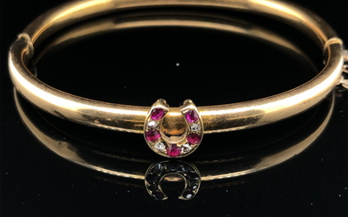 AN ANTIQUE BANGLE SET WITH A RUBY AND DIAMOND HORSESHOE. THE HINGED BANGLE UNHALLMARKED, ASSESSED AS