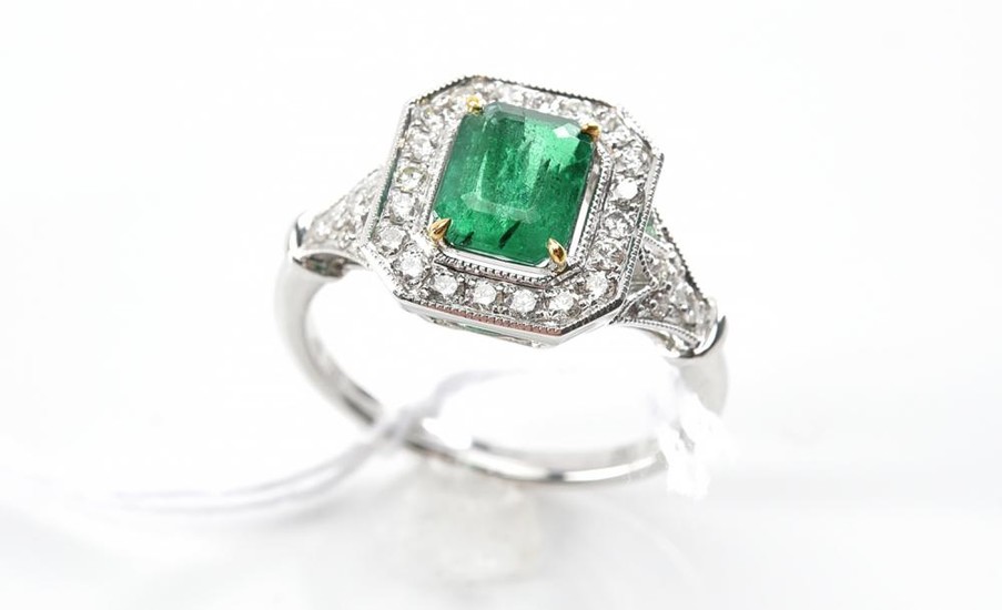 AN EMERALD AND DIAMOND DRESS RING - Featuring an emerald cut emerald weighing 1.10ct, surrounded and shouldered by round brilliant c...