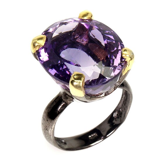 An amethyst ring set with an oval-cut amethyst, mounted in black rhodium and gold plated sterling silver. 19×12 mm. Size 58.