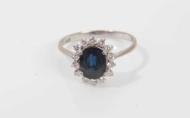 Sapphire and diamond cluster ring with an oval mixed cut blue sapphire measuring approximately, surrounded by 14 brilliant cut diamonds in claw setting on 14ct gold shank