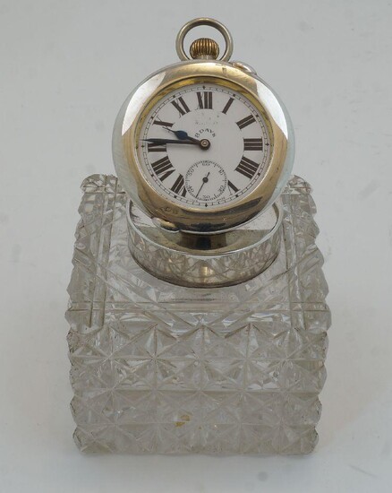 A George V square cut glass and silver-mounted inkwell, Birmingham, 1925, James Swann & Son., the silver cover inset with pocket watch, having white enamel dial with Roman numerals and subsidiary seconds dial, marked 8 DAYS to dial, 10cm high