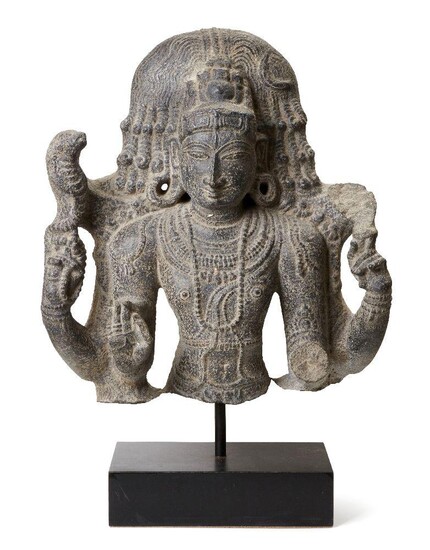 A black stone sculpture of Shiva, India, 19th century in a 10th century style, carved wearing a bejewelled tiered tiara, the elegant rounded face with almond eyes, straight nose and bow lips, and flanked with pendulous earlobes, wearing strands of...