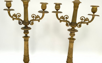 Coppia di candelieri a tre fiamme in bronzo dorato con braccia mosse, fusto a colonna scanalata su base circolare decorata...