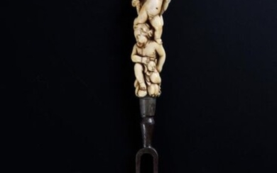 Two-toothed steel fork with an ivory handle carved with three overlapping putti holding fruit.