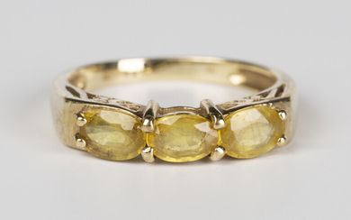 A 9ct gold and yellow gemstone set three stone ring, mounted with a row of three oval cut yellow gem