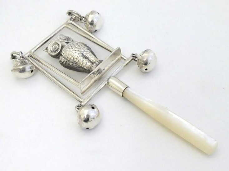 A white metal children's rattle with owl decoration