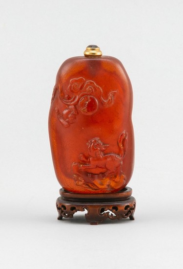 CHINESE CARVED AMBER SNUFF BOTTLE In pebble form, with carved qilin, bat, pearl and cloud decoration. Height 2.5". Replacement stone...