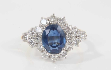 Sapphire and diamond cluster ring with an oval mixed cut blue sapphire measuring approximately 9.5mm x 7.7mm x 3.3mm surrounded by twelve brilliant cut diamonds with a further six diamonds to the s...