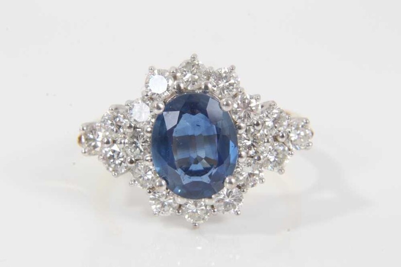 Sapphire and diamond cluster ring with an oval mixed cut blue sapphire measuring approximately 9.5mm x 7.7mm x 3.3mm surrounded by twelve brilliant cut diamonds with a further six diamonds to the s...
