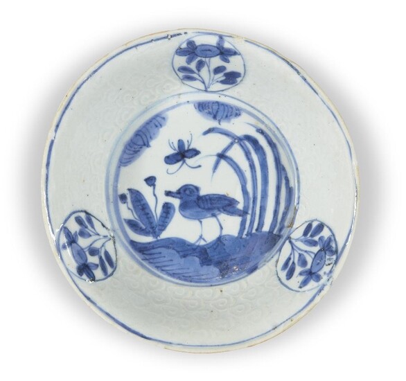 A Chinese porcelain blue and white ko-sometsuke 'bird' dish, Tianqi period, the interior painted with a lone bird perched on the banks of river, the cavetto with moulded lingzhi clouds and three raised panels enclosing flowers, 15.3cm diameter 明天啟...