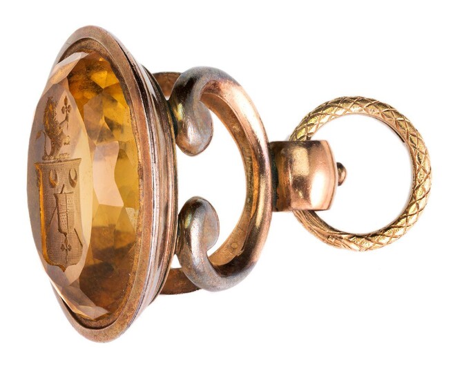 A large early 19th century gold mounted citrine fob seal, the oval citrine matrix with an intaglio engraved armorial, to an open work scroll bracket handle with ouroboros engraved split ring, c.1820