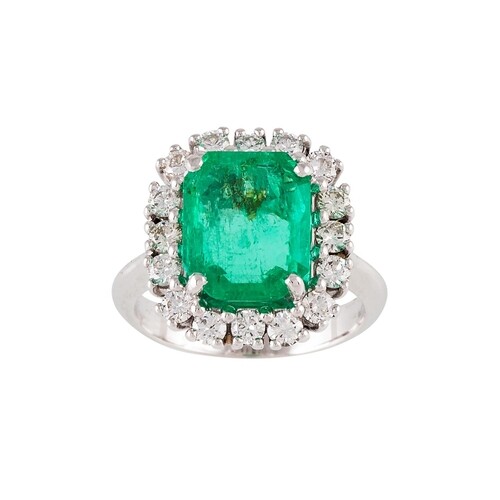 AN EMERALD AND DIAMOND CLUSTER RING, the trap cut emerald to...
