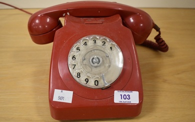 A vintage red rotary telephone.