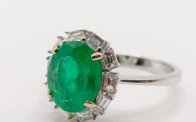 An 18ct white gold ring, set with an oval emerald and surrou...