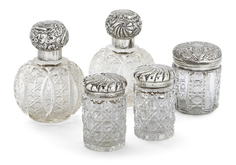 Five silver mounted glass vanity vessels, including: a pair of globular cut glass examples, London, probably c.1900, Charles Fox & Co., (marks rubbed), both with cut glass stoppers and repousse decorated screw caps, 14.3cm high; a pair of Victorian...