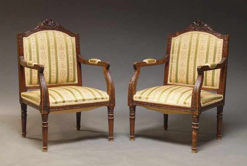 A pair of Louis XVI style stained beech fauteuils, 20th Century, the shaped backs with carved crest rail, upholstered in striped silk material, on tapering fluted legs (2)