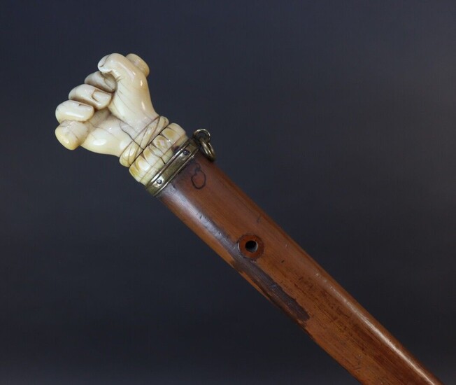 Cane with reed shaft. Pommel showing an ivory hand holding a stick. Mounted with a brass ring. Height 84,5 cm
