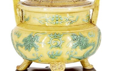 A Chinese porcelain yellow and green-enamelled 'dragon' censer and cover, 18th century, the exterior decorated with a pair of four-clawed dragons converging on a flaming pearl, the tripod legs moulded as feet protruding from the mouths of mythical...