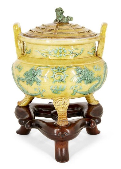 A Chinese porcelain yellow and green-enamelled 'dragon' censer and cover, 18th century, the exterior decorated with a pair of four-clawed dragons converging on a flaming pearl, the tripod legs moulded as feet protruding from the mouths of mythical...