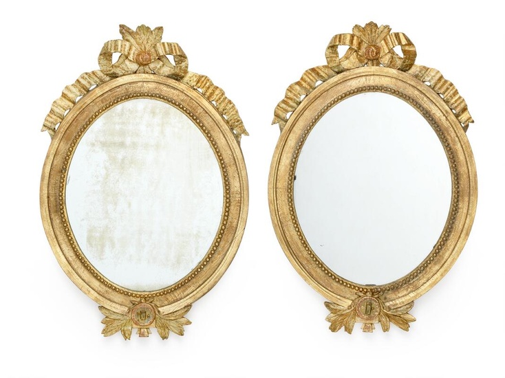 A pair of oval Gustavian giltwood mirrors, each carved with openwork bow...