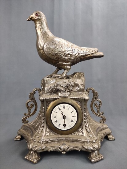 A table clock with a fully plastic dove, on a floral decorated base, clock face with Roman numbers